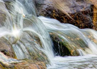 A blurred image of a cascading waterfall over rocks, capturing the shimmering motion of water in soft hues